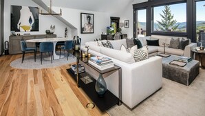 Una sala moderna con un sofá blanco, un comedor con sillas azules y un ventanal con vistas al exterior.