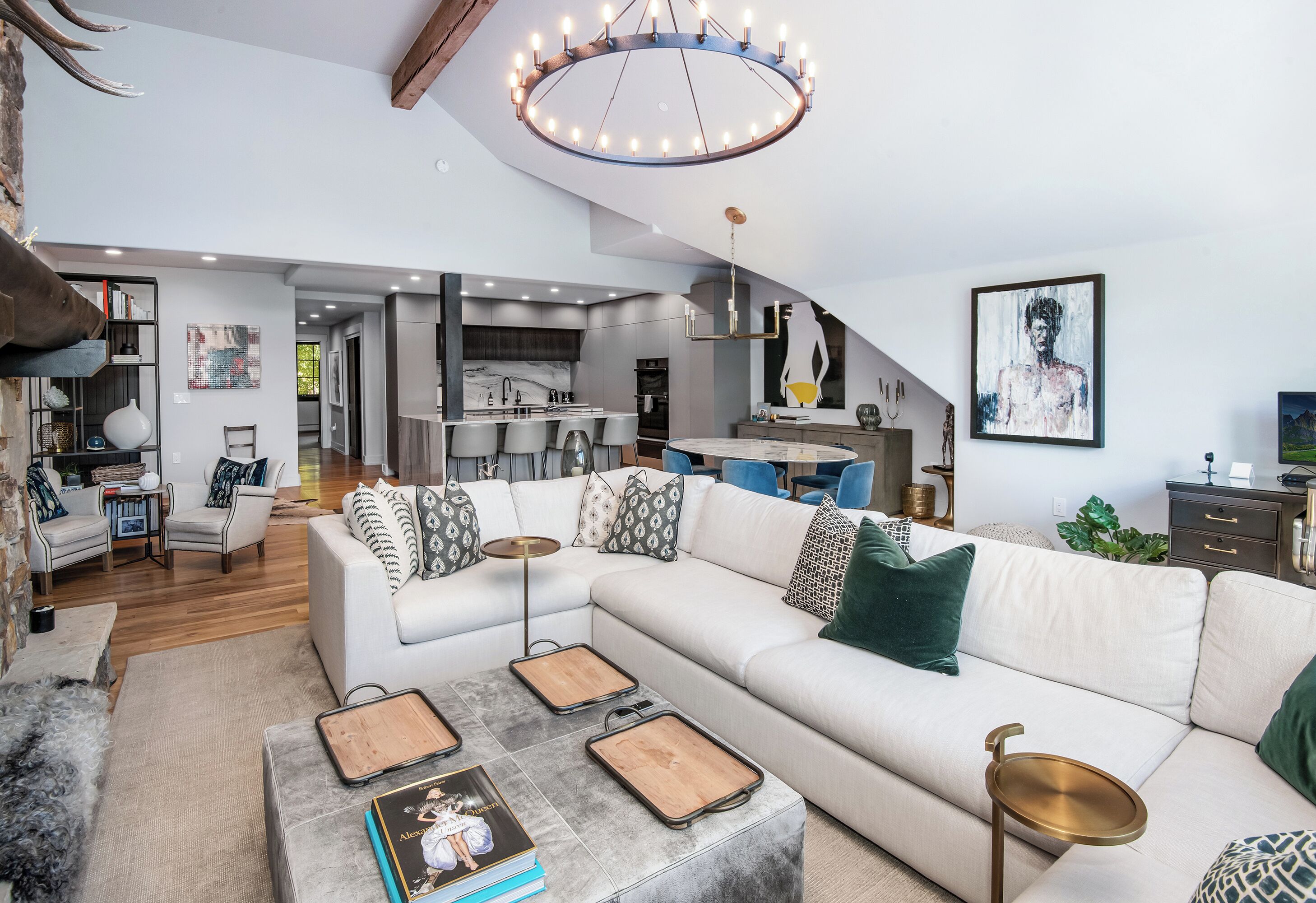 A modern living room with a sectional sofa, a coffee table with trays, and a dining area with blue chairs.