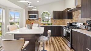 A modern kitchen with a central island, dark wood cabinets, a built-in oven, and a microwave.