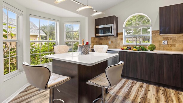 A modern kitchen with a central island, dark cabinetry, a microwave, and a window overlooking greenery.