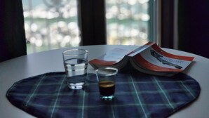 A table with a placemat, two glasses of water, and a glass of dark liquid, possibly coffee, with a magazine or book on it. - SEA DREAM PALACE 1 (Trani)