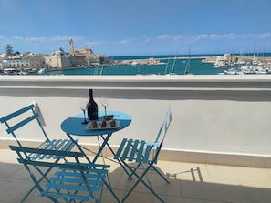 A balcony with a table set for two, a bottle of wine, and a plate of food.