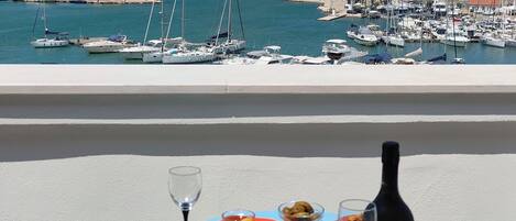 A balcony with a table set for a meal, overlooking a marina with boats and a historic stone wall.