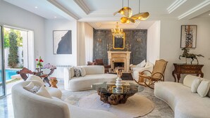 A spacious living room with a fireplace, comfortable seating, and a view of a pool. - Villa Victoria La Marsa (La marsa)