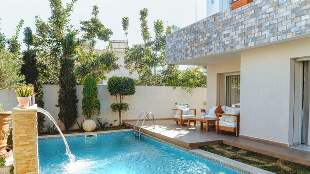 A swimming pool with a water feature, surrounded by a patio with outdoor furniture and a brick wall. - Villa Victoria La Marsa (La marsa)