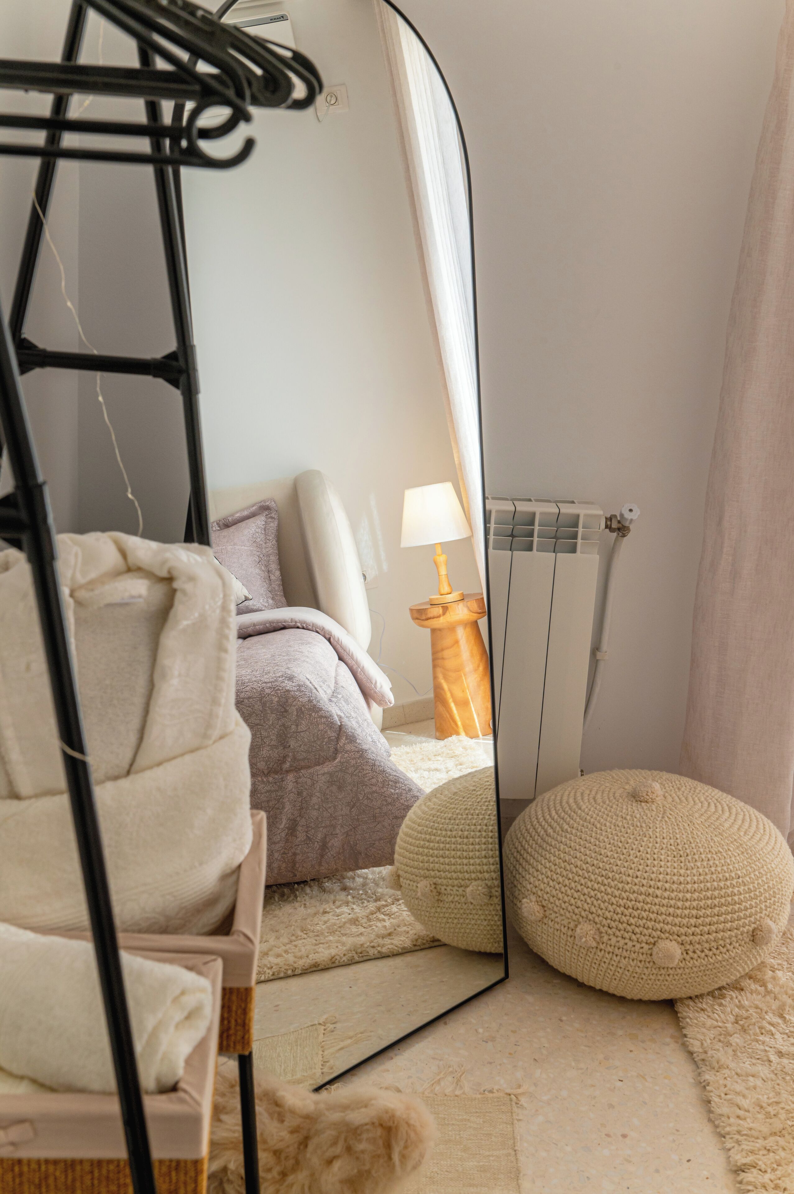 Een slaapkamer met een bed, een spiegel, een radiator en een nachtkastje met een lamp.