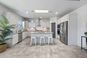 A modern kitchen with white cabinets, a central island with stools, stainless steel appliances, and a skylight.