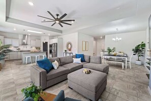 A modern living room with a sectional sofa, ottoman, and a dining area with a table and chairs. - Texas Modern 4BR 3BA Home Gazebo Spacious Yard (Canutillo)
