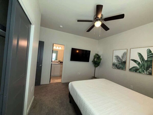 A bedroom with a bed, a ceiling fan, a TV, and artwork on the wall.