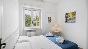 Ein Hotelzimmer mit Bett, Fenster, Heizkörper, Lampe und zwei Bildern an der Wand.