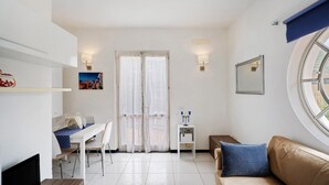 Ein Zimmer mit Esstisch, Stühlen, einer Couch, einem Fernseher, einem Fenster und einer Tür mit Vorhängen.