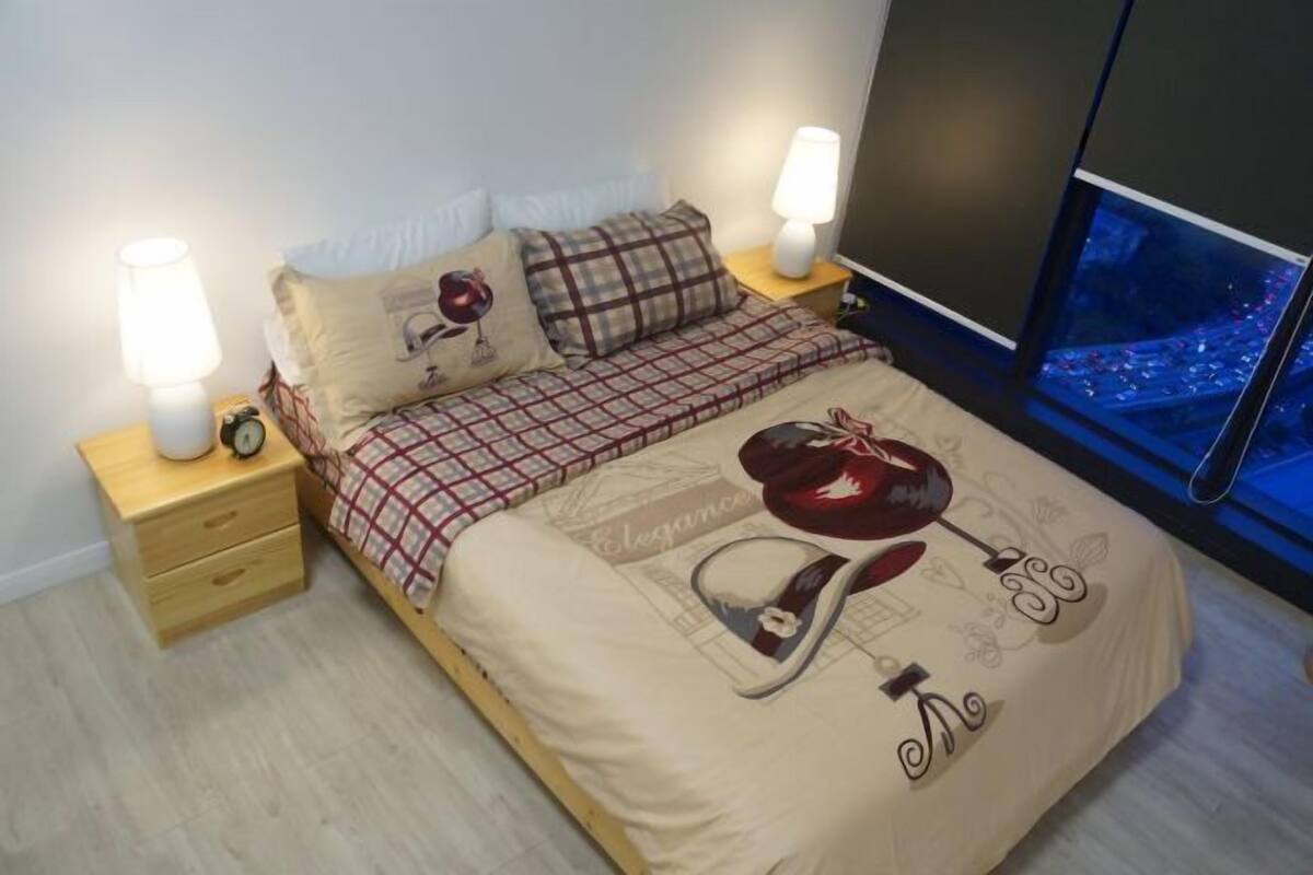 Un dormitorio con una cama, dos lámparas de noche, una mesita de noche y una ventana con vista a la ciudad.