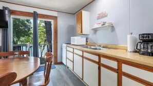 Een kleine keuken met een houten tafel en stoelen, een ingebouwde magnetron, een koffiezetapparaat en een raam met gordijnen.