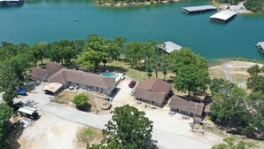 An aerial view of a lakeside property with multiple buildings, a swimming pool, and docked boats.