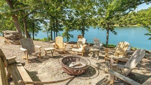 A lakeside seating area with Adirondack chairs and a fire pit.