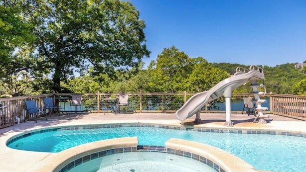 A swimming pool with a slide, lounge chairs, and a hot tub.