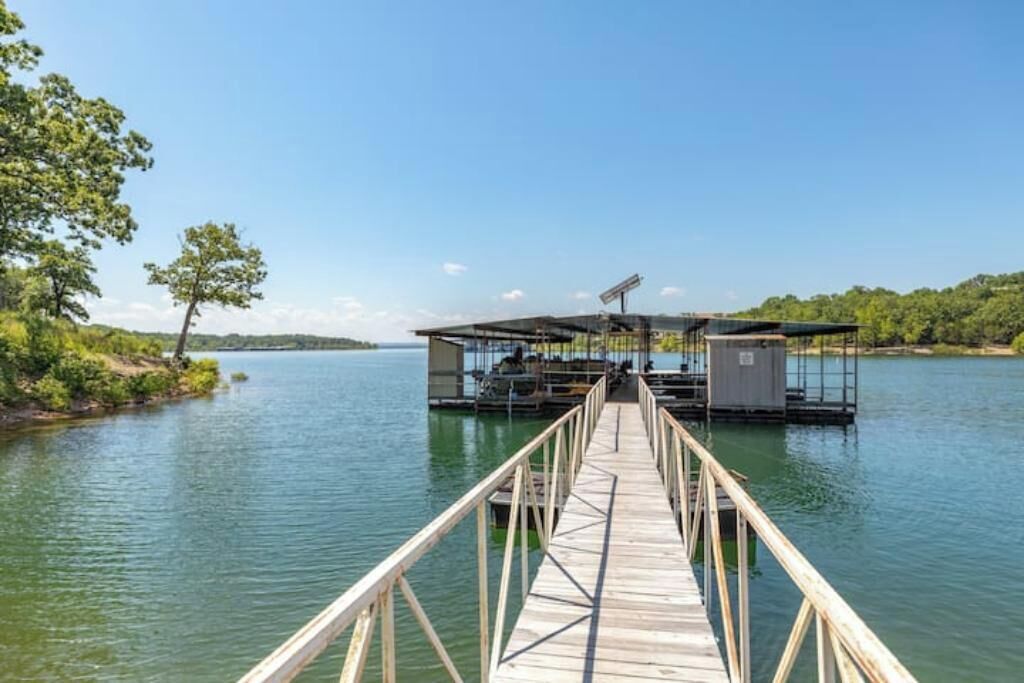 A wooden dock leading to a floating structure with a roof, surrounded by calm water and greenery.