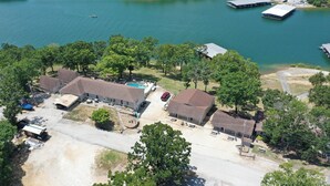 Vue aérienne d’une propriété au bord du lac, comprenant plusieurs bâtiments, un quai et une piscine.