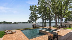 A swimming pool with lounge chairs and a barbecue area, surrounded by trees and a view of a lake. - The Retreat at Sunrise Cove (Sherrills Ford)