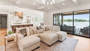 A spacious living area with a large sectional sofa, a dining area, and a view of a body of water through large windows. - The Retreat at Sunrise Cove (Sherrills Ford)