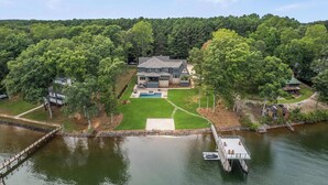 A large house with a swimming pool, surrounded by a well-maintained lawn and trees, with a dock and boat in the foreground. - The Retreat at Sunrise Cove (Sherrills Ford)