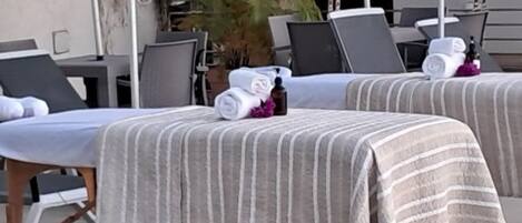 Two spa beds with striped towels and bottles, a potted plant, and outdoor umbrellas.
