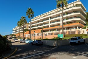 Ein mehrstöckiges Hotel mit Balkonen, parkenden Autos und Palmen.