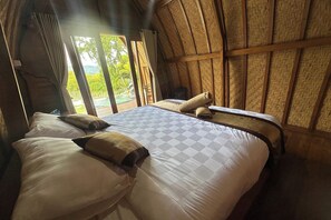 A room with a large bed, a small table, and a view of greenery outside. - Nirwana Kintamani By Zuzu (Kintamani)