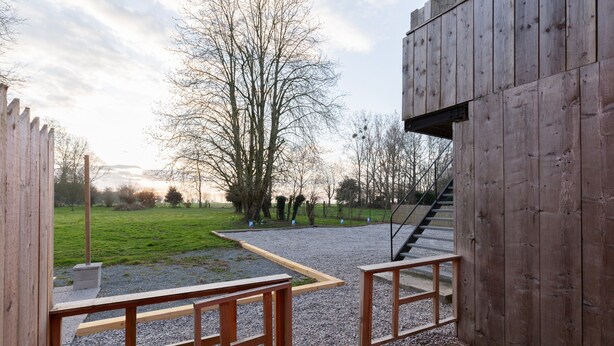 Ein Holzgebäude mit einer Treppe, die zu einem Kiesplatz führt, umgeben von Bäumen und einer Wiese.