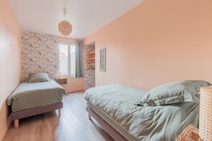 Une chambre avec deux lits, une fenêtre, un mur orné d’un motif floral et un luminaire suspendu.