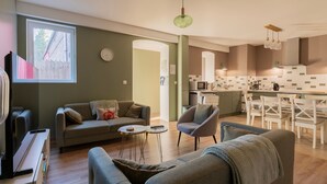 Ein modernes Wohnzimmer mit Sofa, Sessel und Couchtisch, eine Küche mit weißen Schränken und ein Essbereich mit weißen Stühlen.
