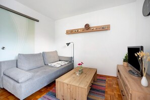 Un salon moderne avec un canapé gris, une table basse en bois, un téléviseur posé sur un meuble en bois et une étagère murale ornée de tableaux.