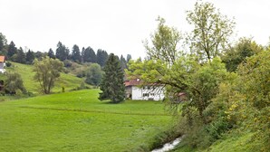 A rural landscape with a house, a stream, and surrounding greenery. - Holiday Apartment 'Am Mühlbach' with Shared Garden, Balcony and Wi-Fi (Marktoberdorf)