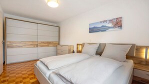 A bedroom with a bed, wooden headboard, bedside tables, a wardrobe, and a wall-mounted picture. - Holiday Apartment 'Am Mühlbach' with Shared Garden, Balcony and Wi-Fi (Marktoberdorf)