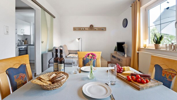 A dining area with a table set for two, a vase with flowers, and a variety of food items. - Holiday Apartment 'Am Mühlbach' with Shared Garden, Balcony and Wi-Fi (Marktoberdorf)