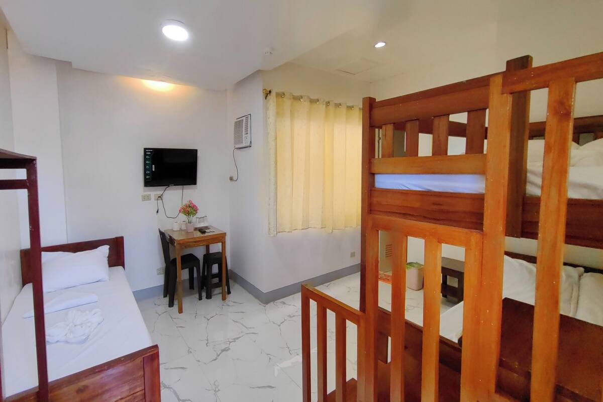 A room with bunk beds, a desk, a television, and a window with curtains.