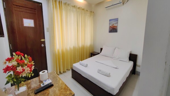 Habitación de hotel con cama, mesita de noche, control remoto, un jarrón de flores y cortina.