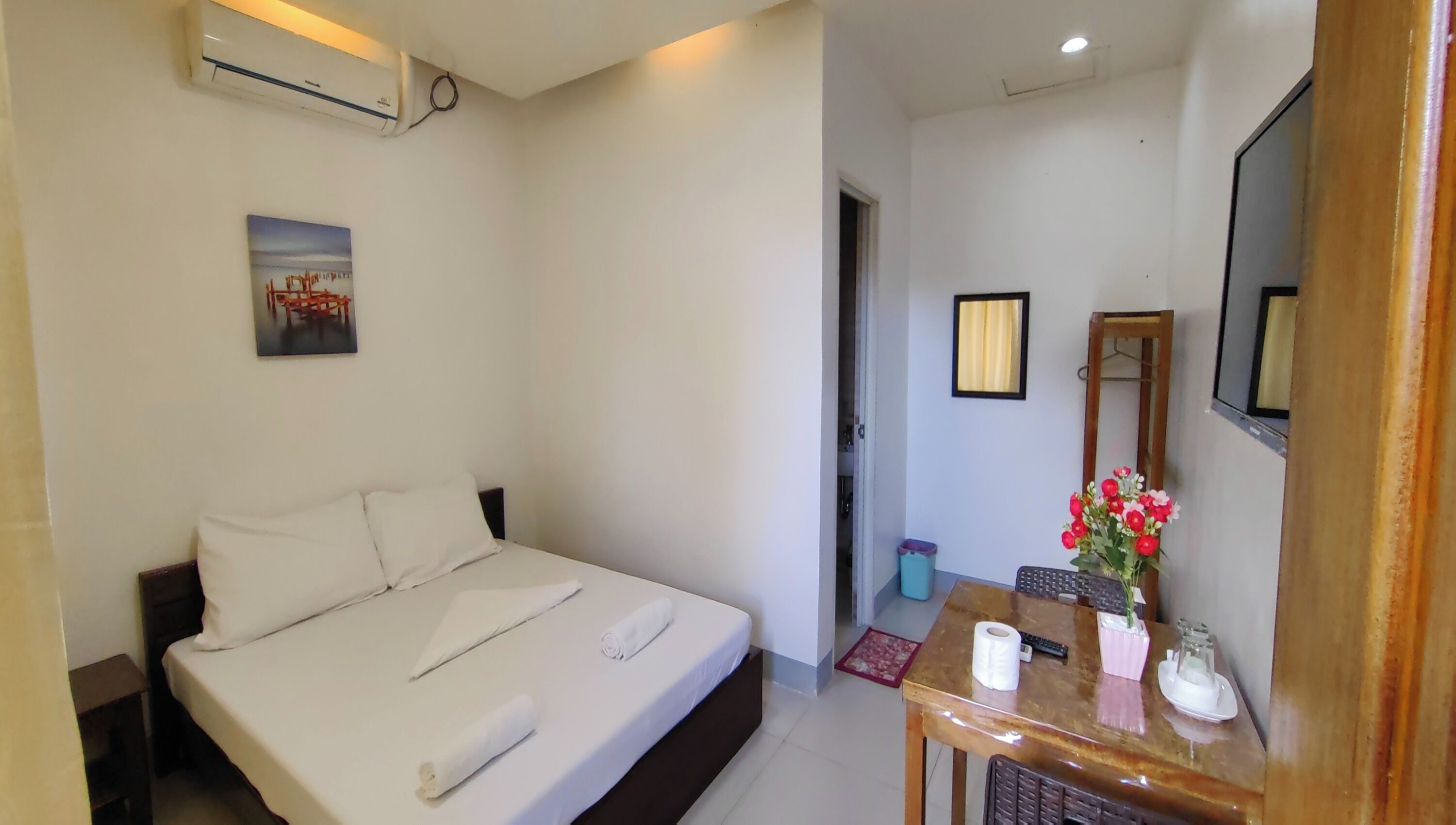 A neatly made bed with white linens, a small table with a vase of flowers, and a mirror on the wall.