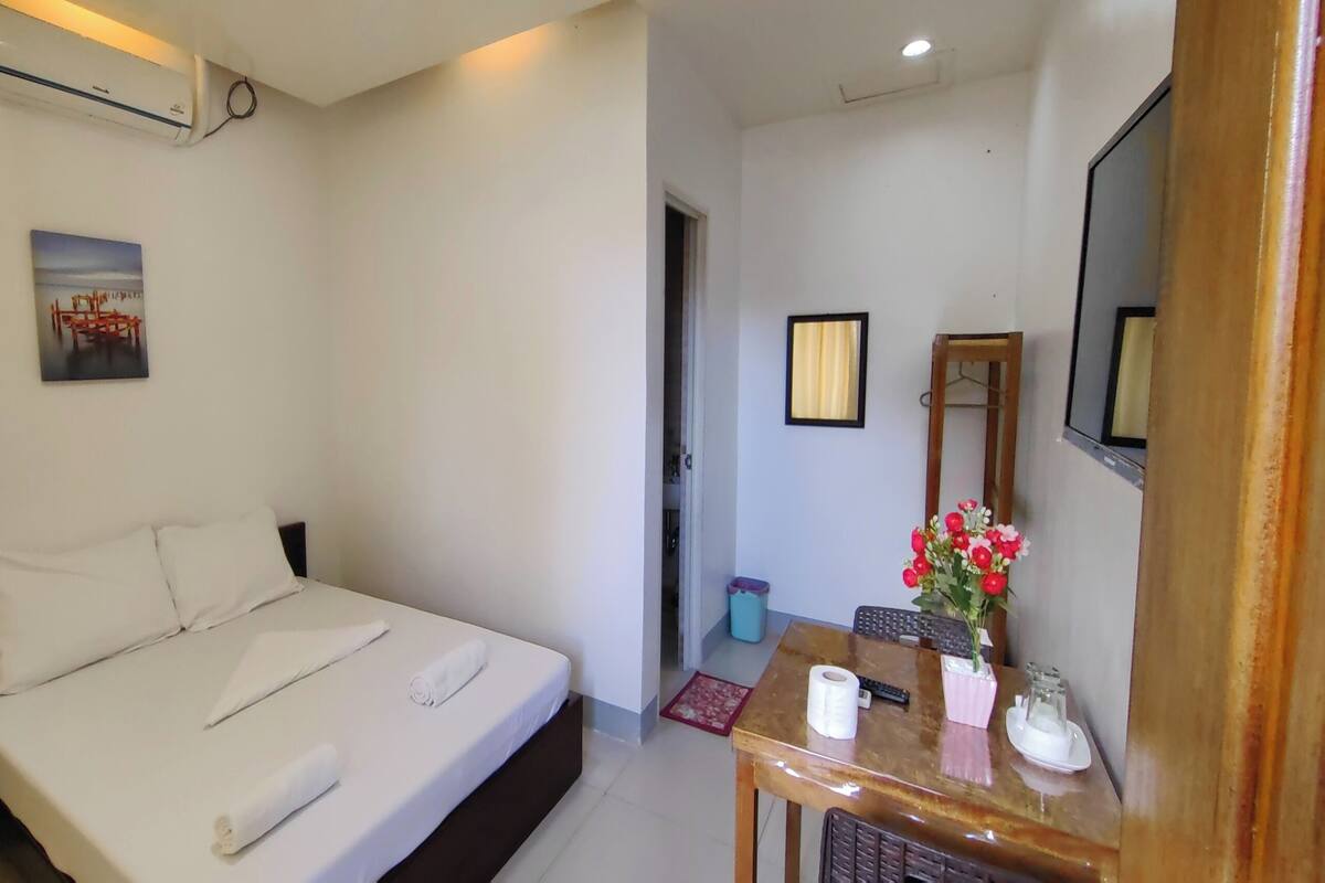 A neatly made bed with white linens, a small table with a vase of flowers, and a mirror on the wall.