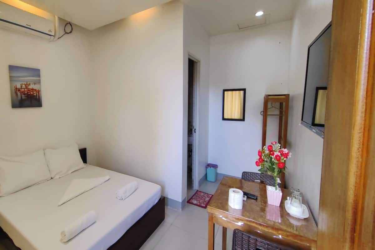 A neatly made bed with white linens, a small table with a vase of flowers, and a mirror on the wall.