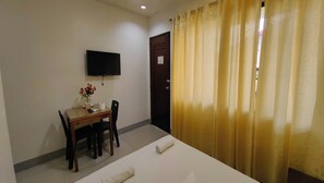 A hotel room with a bed, a desk with a chair, a flat-screen TV mounted on the wall, and a door with a curtain. - Pring Pension House Puerto Princesa By Zuzu (Puerto Princesa)