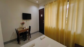 Quarto de hotel com cama, escrivaninha com cadeira, TV de tela plana na parede e porta com cortina.
