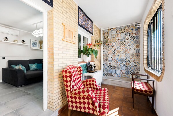 Una sala de estar con un sofá negro, un sillón a cuadros rojo y blanco, una mesa blanca con una planta y una pared decorada.