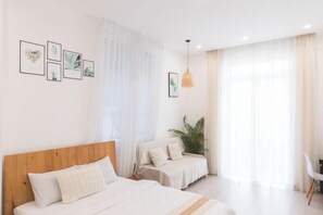 A hotel room with a wooden headboard bed, a smaller bed with a headboard, a potted plant, a desk with a chair, and framed botanical prints on the wall. - THE ARIX House & Studio (Dalat)