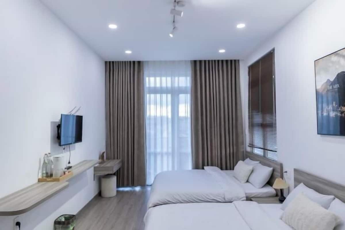 Ein Hotelzimmer mit Bett, Nachttisch, Fernseher, Vorhängen und einem Fenster.