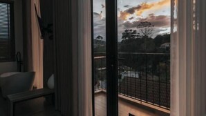 Ein Zimmer mit großem Fenster, einer Bank und Blick auf einen Balkon mit Geländer.