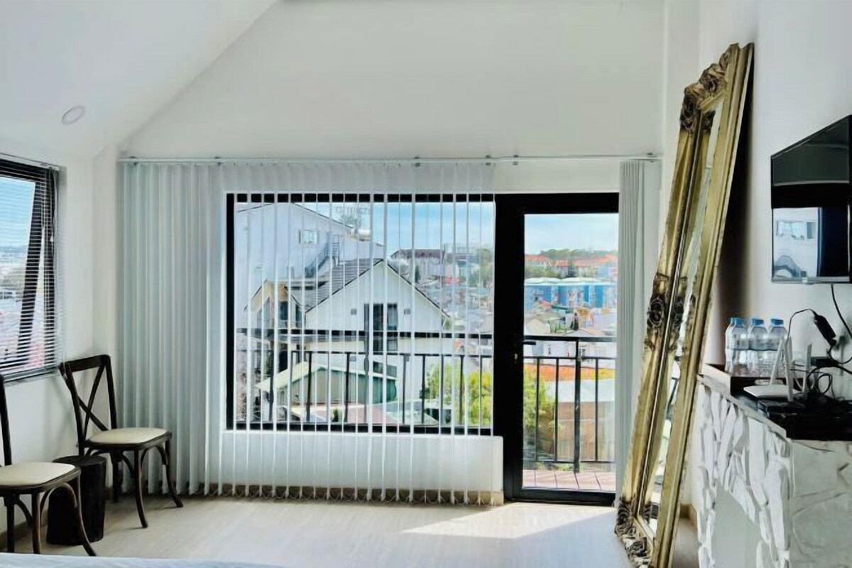 A modern room with a large window, a view of buildings, a mirror, and a TV.
