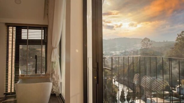 Ein Zimmer mit großem Fenster, Blick auf eine Stadtlandschaft und einem Balkon mit Geländer.