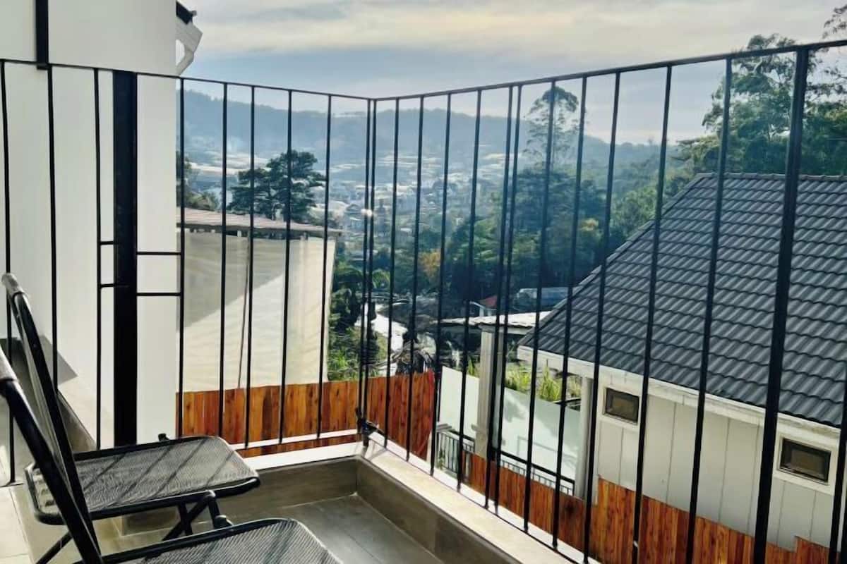 Ein Balkon mit Metallgeländer, einem Stuhl und Blick auf Stadt und Grünflächen.