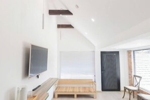 A modern room with a wooden bench, a TV mounted on the wall, a door, and a window with blinds. - THE ARIX House & Studio (Dalat)
